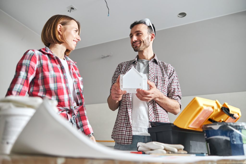 Low angle of a handsome architect with a miniature house in his hands smiling at his assistant