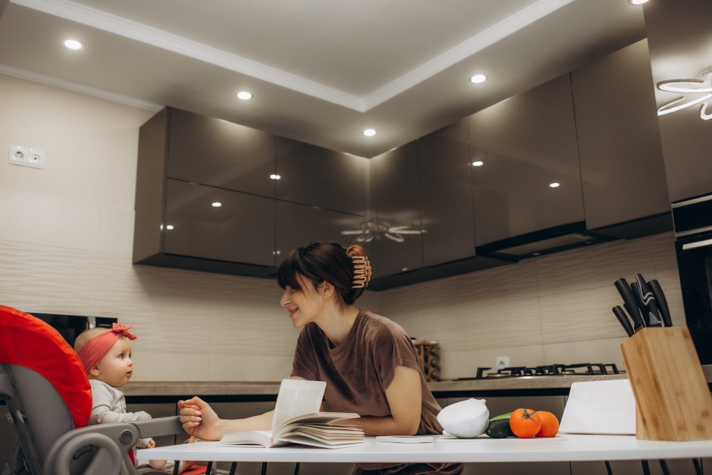 Beautiful young brunette woman in dress with baby in the kitchen at home