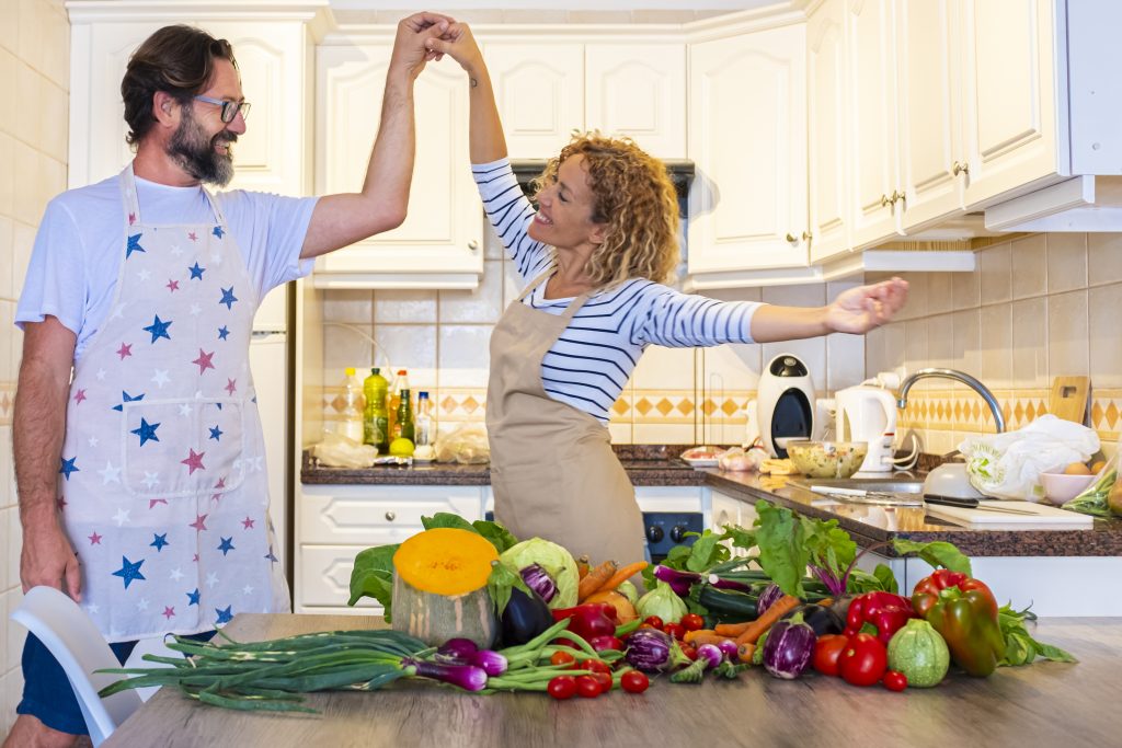 Happy adult couple dance and have fun together in the kitchen with healthier cooking ingredients