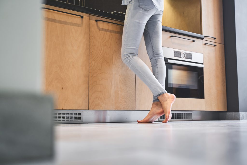Cropped photo of a young housewife in denim pants standing barefoot on the tile floor
