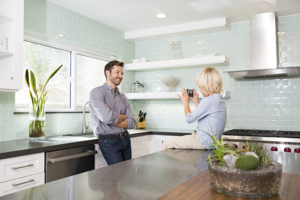 Son taking cell phone picture of father in kitchen